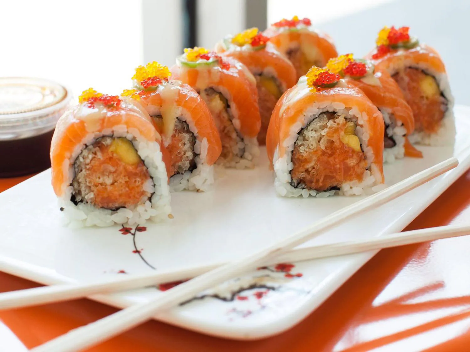 Salmon sushi roll with red and yellow fish roe, soy sauce, and chopsticks on white plate at Sushi Yoshi，a Japanese Restaurant in Brooklyn