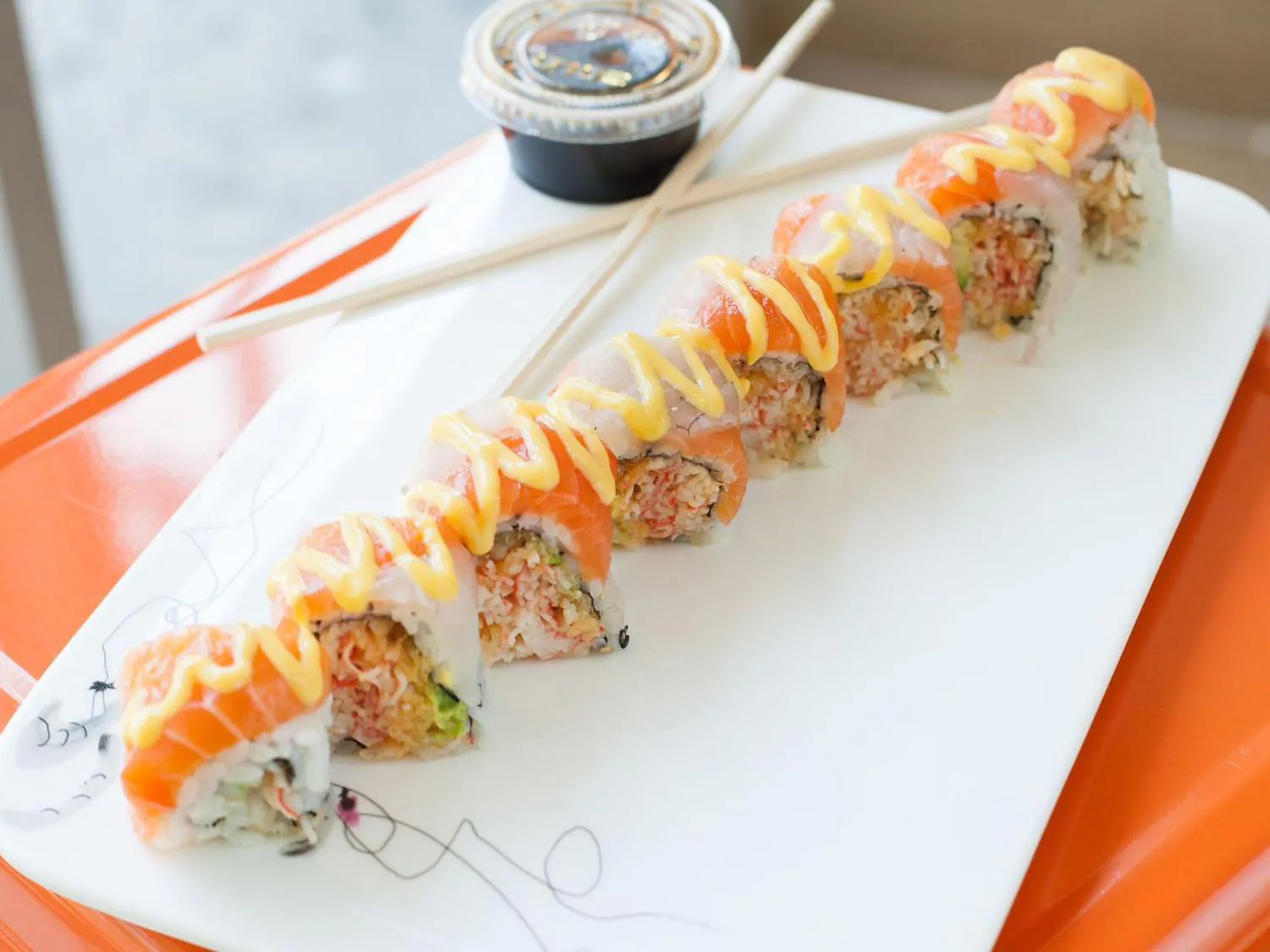 Salmon sushi roll with yellow sauce and chopsticks on white plate at Sushi Yoshi，a Japanese Restaurant in Brooklyn