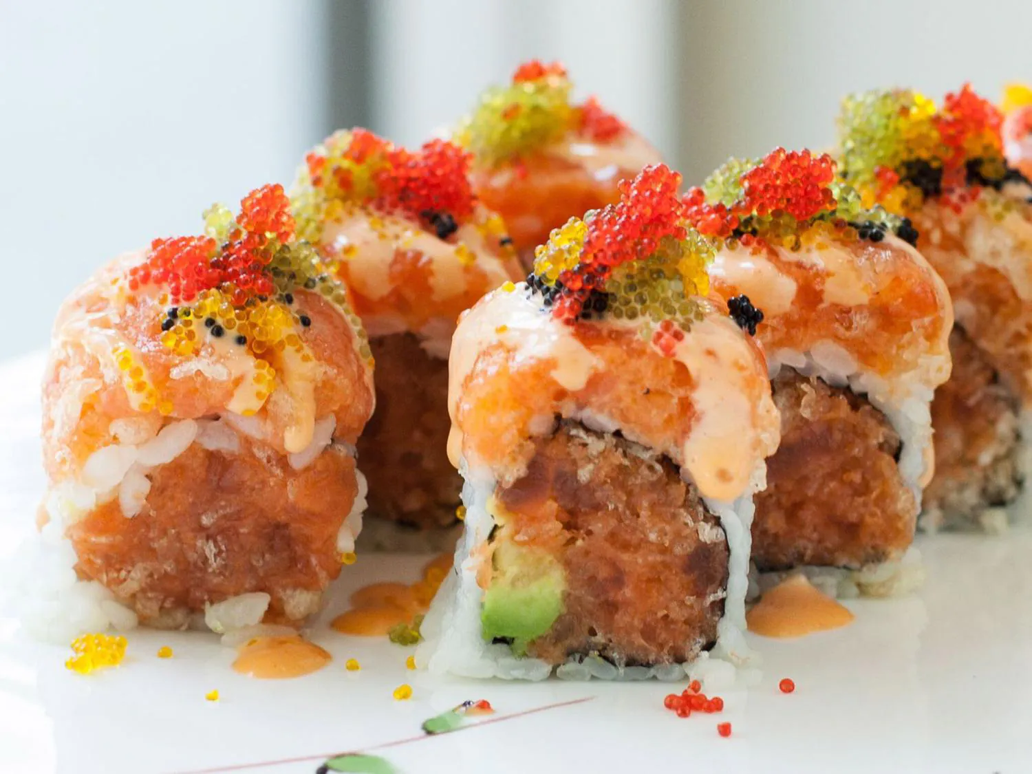 Sushi roll with spicy salmon, avocado, and colorful fish roe on white plate at Sushi Yoshi，a Japanese Restaurant in Brooklyn